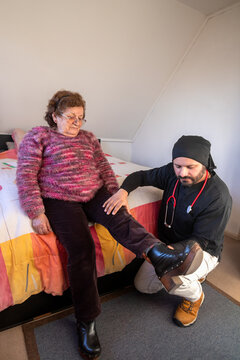 A young male doctor on a house call examines the joints of an elderly woman