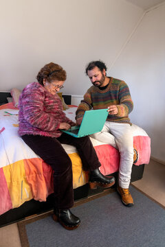 A man helps his elderly mother use her laptop and browse the web from home