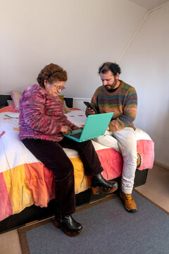 An elderly woman works on a laptop while her son helps her make a bank transfer from home