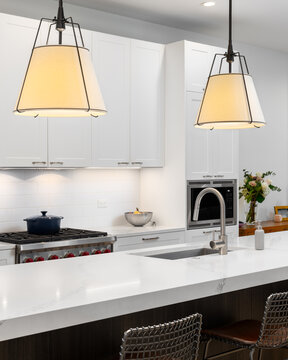 A kitchen detail with large lights hanging over the island with marble countertop, white and dark wood cabinets, and subway tile backsplash.