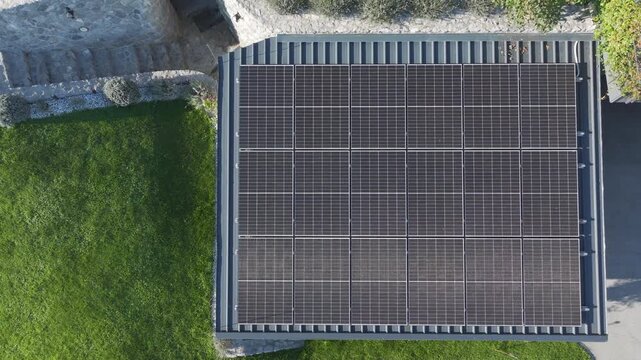 AERIAL TOP DOWN: Rooftop solar panels on a residential property surrounded by green lawn and garden paths in the countryside. Domestic renewable energy, electricity production and sustainable living.