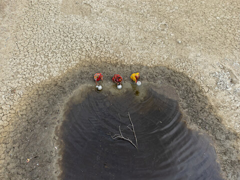 Shyamnagar, Khulna Division, Bangladesh - 25 April 2025: Aerial view of three women in colorful saris collecting water from a small, muddy pool in a parched, cracked landscape.