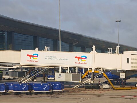 TotalEnergies advertising display on an airport jet bridge at Bengaluru International Airport with IndiGo ground equipment on the tarmac tarmac
