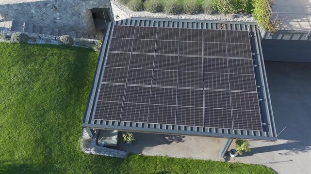 AERIAL: Modern rooftop covered with solar panels on a sunny countryside property, surrounded by green lawn, garden landscaping and stone walls. Domestic renewable energy production and sustainability.