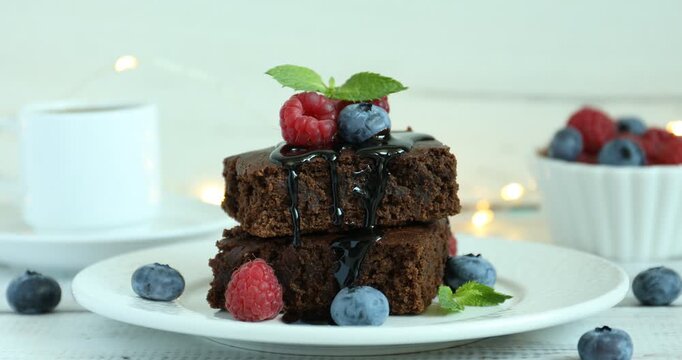 Woman putting mint onto pieces of delicious brownie with fresh berries at table, closeup
