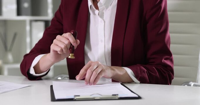 Notary checking and stamping documents at white table in office, closeup
