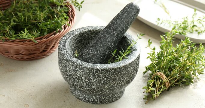 Woman putting fresh thyme into mortar with pestle at light table, closeup