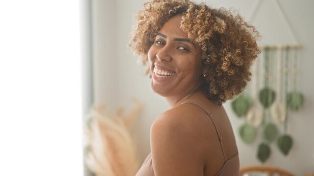 Woman smiling, cleavage and shoulder shown in thin tank top facing camera in studio; confidence self care.