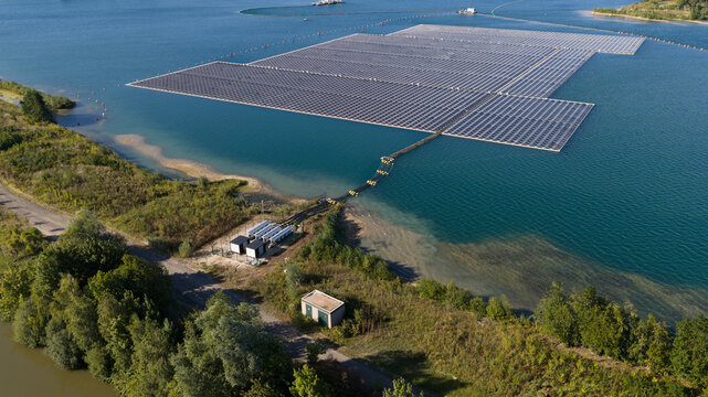 Aerial view of a large floating solar farm on a calm lake, with rows of photovoltaic panels connected to the shore, surrounded by green vegetation in Echteld, Gelderland, Netherlands.