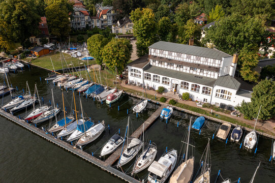 Aerial view of Yachtclub Wendenschloss e.V. with numerous sailboats moored at the pier, surrounded by lush trees and buildings in Berlin, Berlin, Germany.