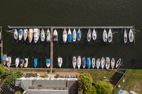 Aerial view of Yachtclub Wendenschloss e.V. with numerous sailboats and motorboats moored at wooden piers in Berlin, Berlin, Germany.