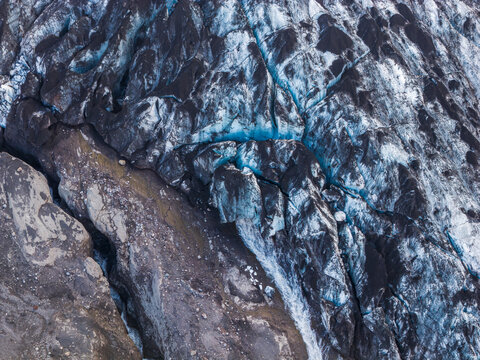 Aerial view of the rugged glacier in Thorsmork with deep blue ice crevasses and dark volcanic ash deposits in Rangarthings eystra, Iceland.