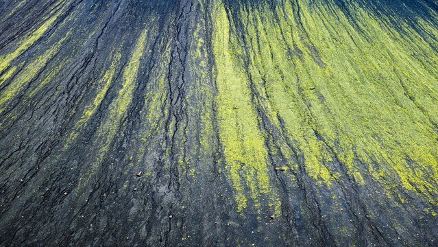 Aerial view of the volcanic slopes of Faxi mountain featuring dark basaltic soil contrasted by vibrant green moss patterns in the Icelandic highlands, Skaftarhreppur, Iceland.