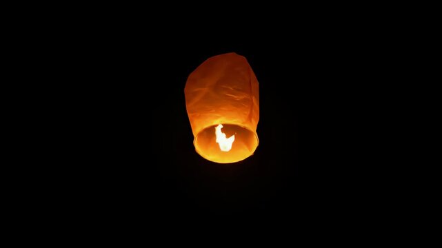 Glowing orange paper lantern floating in night sky.