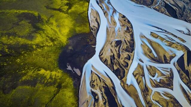 Aerial view of the braided Tungnaa river flowing through vibrant green mossy terrain and dark volcanic landscape in Skaftarhreppur, Iceland.
