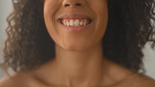 Woman with curly hair smiling showing teeth and exposed gums, bare shoulders visible in studio under soft light; happiness confidence warmth.