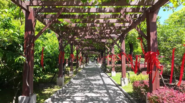 Wooden trellis walkway decorated with red ribbons in sunny park.