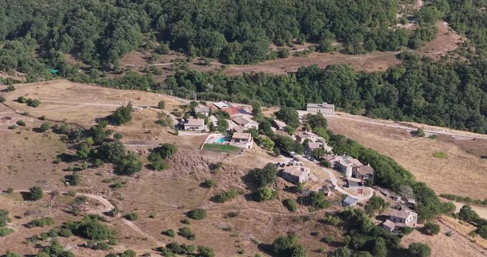 Aerial view of a small rural village with stone houses and a swimming pool nestled in the hilly landscape of Spoleto, Umbria, Italy.