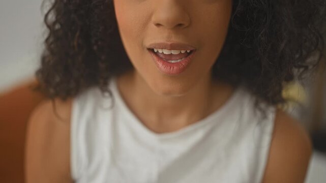 Woman finger to lips shushing in studio closeup, hand and mouth visible with white tank top and painted nails; secrecy intimacy.