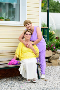 Authentic portrait of two senior russian sisters 80 and 75 years old sitting on a bench near a house porch in a summer garden in Russia
