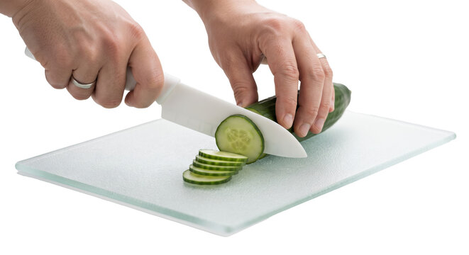 PNG cut out isolated background. A close-up shot of a person's hands using a white knife to slice a fresh green cucumber into thin rounds on a glass cutting board against an isolated black background.