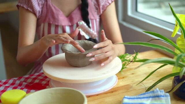 Woman Shaping Clay Bowl by Hand on Pottery Turntable at Wooden Table Indoors
