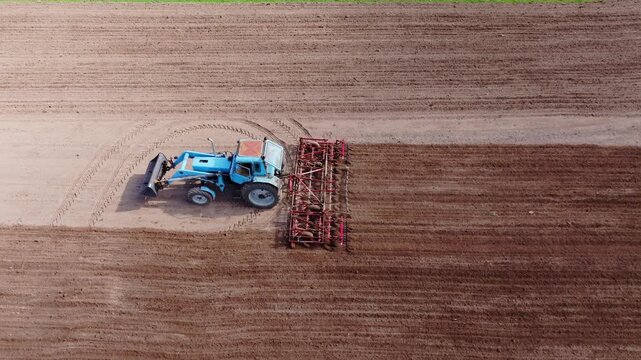 Drone follows working tractor as cultivator prepares long rows of farmland soil