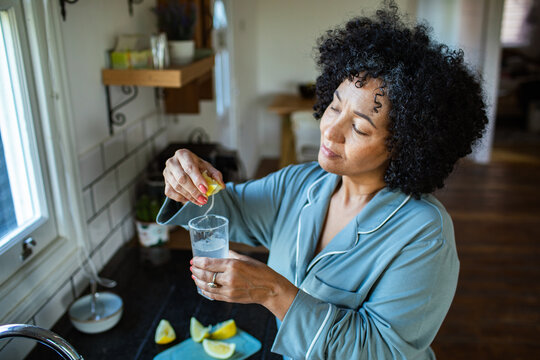 Middle-aged woman squeezing lemon into water at home kitchen