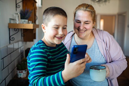 Smiling mother and son looking at smartphone in kitchen