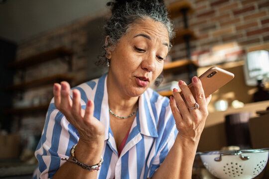 Mature woman using smartphone speakerphone in home kitchen