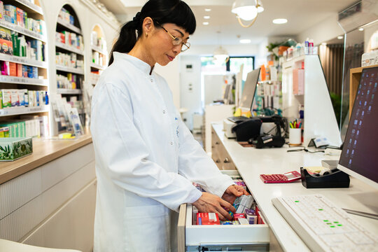 Female pharmacist organizing medications at pharmacy counter