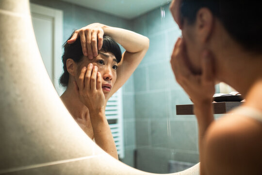 Concerned woman checking under eye skin in bathroom mirror