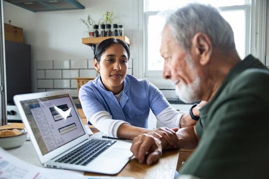 Caregiver helps senior with laptop at home kitchen table