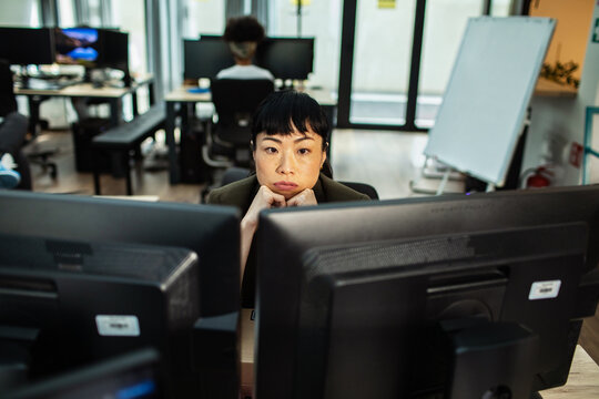 Tired office worker staring at dual monitors in open-plan workspace