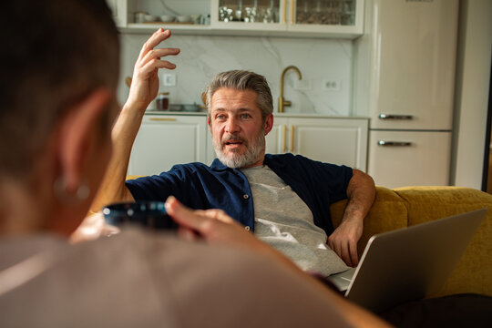 Mature man talking with friend on sofa at home