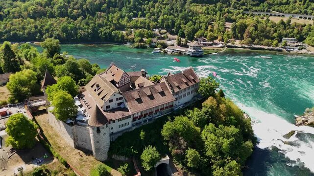 Aerial view of Schloss Laufen beside Rhine Falls near Schaffhausen, Switzerland, with historic architecture, turquoise currents, sightseeing boats and a tunnel below.