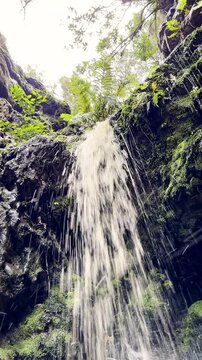 Vertical upward POV as freshwater stream plummets over rock face in mountains