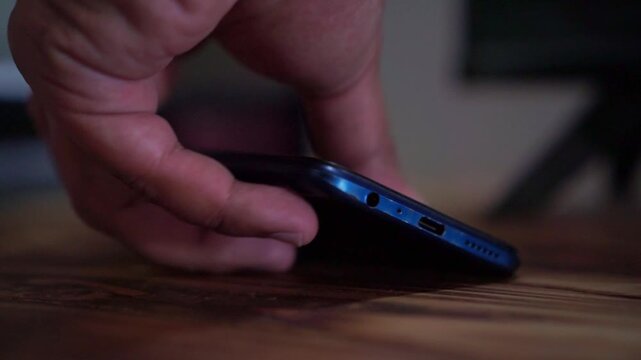 Hand plugging in charging cable to mobile phone, close up view, smartphone charging technology, dark background footage scene.