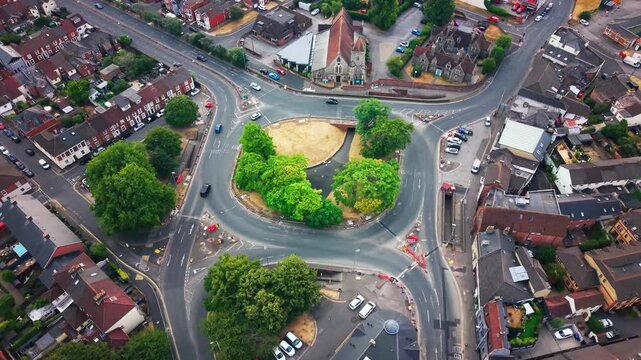 Aerial drone footage looking down on a busy road roundabout in a small English town with a parish church terraced houses and passing traffic