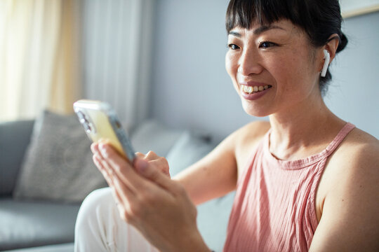 Smiling woman using smartphone with earbuds in living room