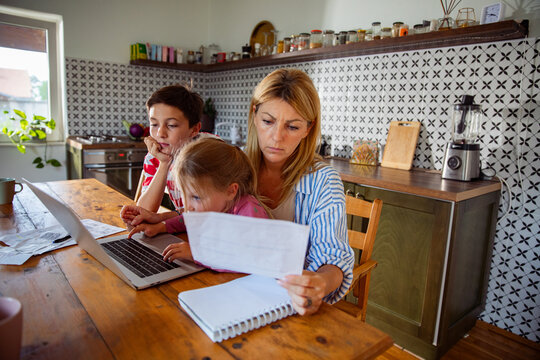 Mother managing family finances with children at kitchen table