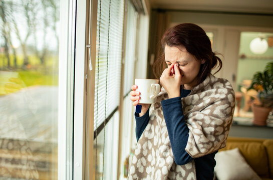 Sick woman with headache drinking tea at home by window