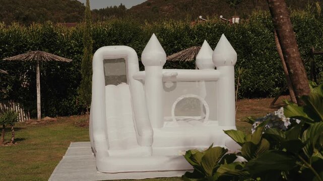 White inflatable bouncy castle with a slide set up on a garden lawn
