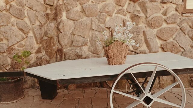 White wooden cart table with a flower basket against a rustic stone wall