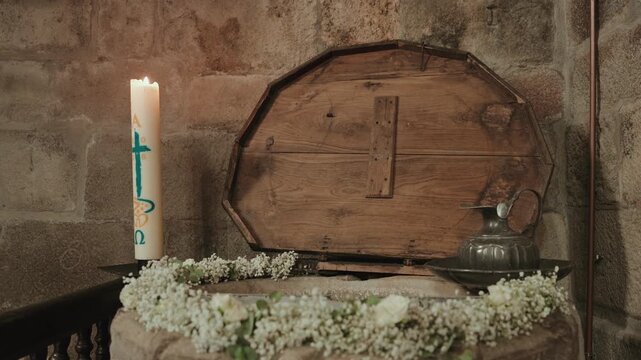 Lit paschal candle and white flowers beside a stone baptismal font in a church