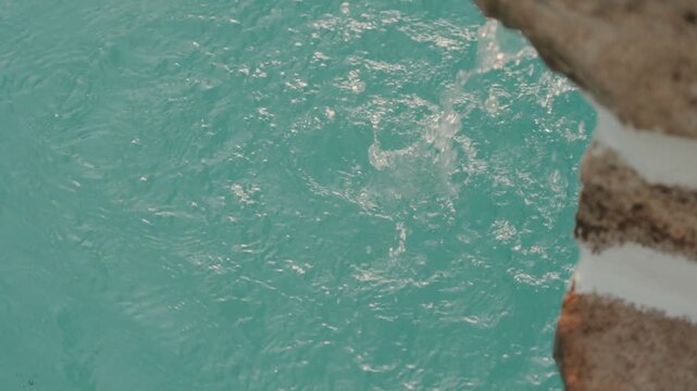 Turquoise pool water rippling beside pale stone steps in warm sunlight