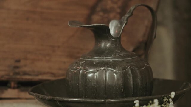 Antique pewter ewer resting in a basin beside white flowers in a church