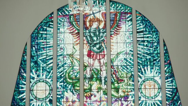 Stained glass window showing a winged archangel in armour standing over a green dragon