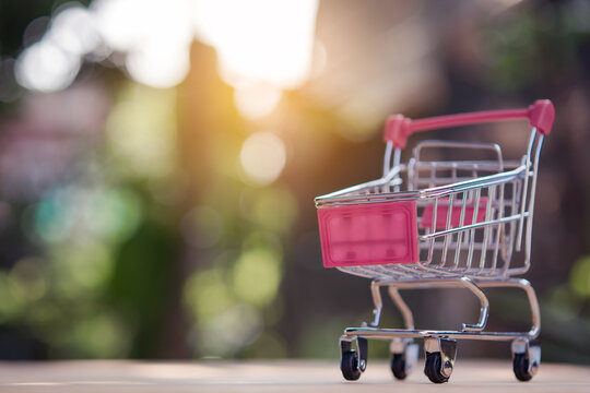 Shopping cart on blurred background, pink handle and basket, miniature metal trolley with wheels