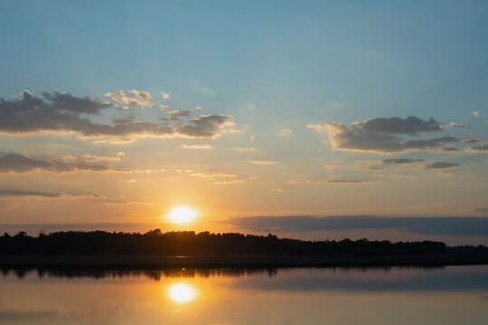 Sunset sky over calm lake with reflection and dark tree line, tranquil evening landscape